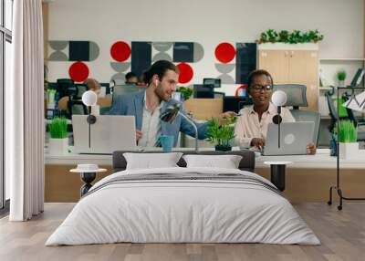 A white handsome man and a gorgeous black women are at their work desks in a large office discussing about work. Wall mural