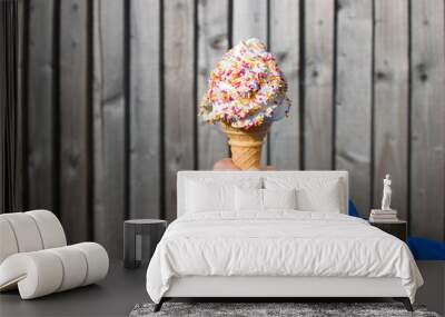 Child's hand holding ice cream cone with sugar sprinkles isolated on neutral wooden fence background with copy space Wall mural