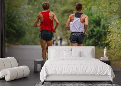 two runners athletes running race together in park road, autumn marathon, fallen yellow leaves on ground Wall mural