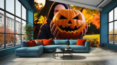 Vibrant high-resolution photo of person holding carved jack-o'-lantern in front of face, with autumn foliage and warm natural light background, generative ai Wall mural