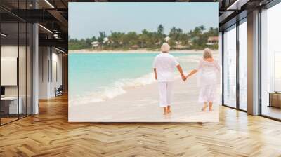 Barefoot Caucasian senior couple in white clothes on a travel resort beach Wall mural