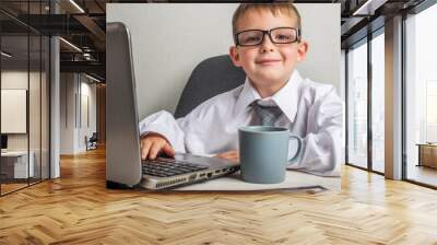 An adorable child is working on a laptop in suit and glasses. Little boss in the office. Children pretend to be adults Wall mural