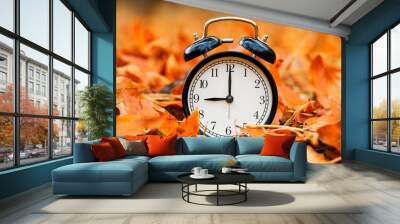 Autumn concept. Alarm clock black on a background of yellow fallen foliage. Fall season Wall mural