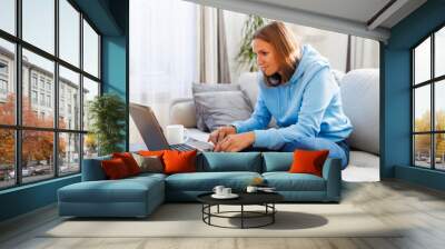 Woman working on a laptop sitting at a table on the couch at home Wall mural