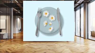 Creative decoration of chamomile flowers on a plate with a knife and fork. Minimal concept of a cut flower on a blue plate with a pastel blue background. Wall mural