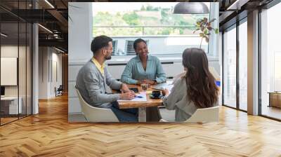 Diverse group of smiling young business people working together on a laptop during a meeting in modern small office. Businessman and businesswoman work on new innovative project of cheap housing. Wall mural