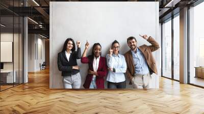 Group of young happy successful business team people pointing finger up and smiling. Freelancers or exchange students showing above and smile looking at the camera.  Wall mural