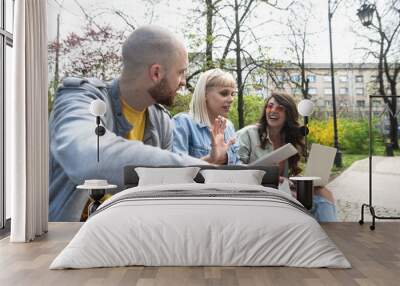 Group of young successful generation z hipster people sitting in park working on laptop computer researching business plan and strategy for digital marketing in which they are experts. Wall mural