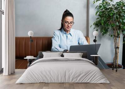 One young businesswoman sitting in cafeteria taking a coffee break while working online on laptop computer. Business female professional occupation e-commerce and remotely finance and economy research Wall mural