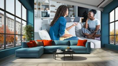 Two young friends and roommates sitting on sofa in their modern cozy studio apartment talking about men. Females conversation about relationships and goals for the future. Wall mural