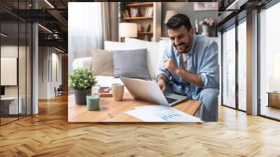 Young business man small startup company owner, working at home, checking the finances on graphs and laptop. Innovative young freelance male calculating costs and expenses of new product strategy. Wall mural