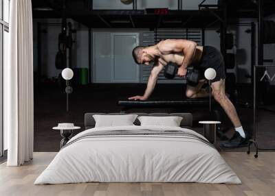 Young concentrated sweaty fit muscular strong man doing hardcore workout training for back muscles with heavy dumbbell weight on the gym bench in the gym, dark image real people exercising Wall mural