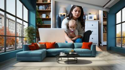 Young female business owner work on laptop from home during maternity leave, running private company with baby in her lap. Businesswoman mother woman with a toddler working at the computer. Wall mural