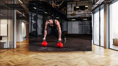 Young strong fit sweaty muscular veteran  man with scars on big muscles doing push ups on two big old heavy kettlebells with his hands for hard core cross workout training on the gym floor and rehab Wall mural