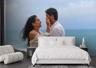  young lovely attractive couple looking at each other, embracing, making love, smiling, cuddling at beach on vacation, holiday, honeymoon, trip to India, Maldives, Asia, foreign beach, cliff, sunset. Wall mural