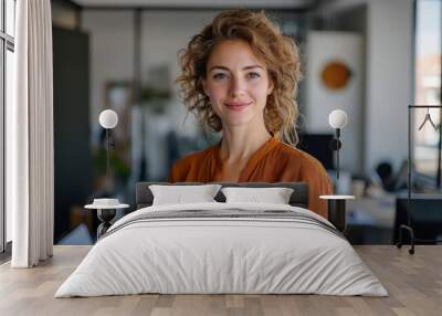 Smiling female designer standing in a modern office, looking directly at the camera with a positive attitude. Wall mural