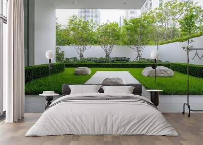 Tranquil modern outdoor garden featuring geometric green hedges lush grass and large stones in a minimalist white walled urban environment creating a peaceful and harmonious atmosphere Wall mural