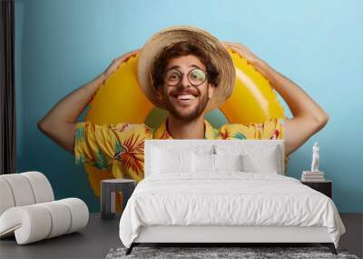 Funny joyful young man set up for summer vacation and looking for good offer from travel agency. Happy guy in summer clothes and with inflatable circle looking into distance on li Wall mural