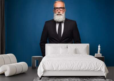 Confident senior bearded man in a suit and tie stand in front of blue isolated background. Fashion posing adult man in fashion glasses and suit Wall mural