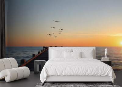 Sunset over calm waters with a wooden pier and birds in the sky Wall mural