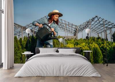 Black watering can made of plastic. Young redhead woman is taking care of garden Wall mural