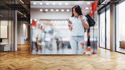 Brunette woman in the supermarket with many of packages and phone in hands have shopping day Wall mural