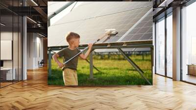 Busy by cleaning the surface. Little boy is with solar panels outdoors Wall mural