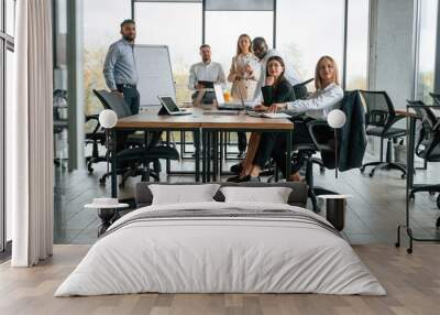 By the table and with whiteboard. Group of office workers are together indoors Wall mural