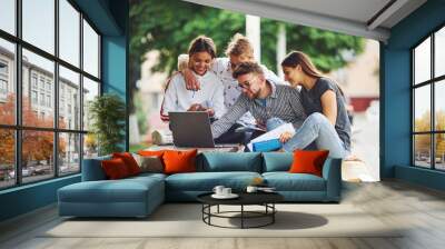 Concentrated at work. With laptop. Group of young students in casual clothes in the city at daytime Wall mural