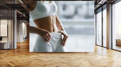 Conception of weight loss, beautiful abs. Young woman with slim body type is in fitness clothes in the studio Wall mural