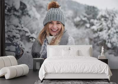 Conception of winter holidays. Cheerful girl in warm clothes playing with snow outdoors near the beautiful forest Wall mural