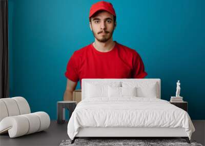 Delivery man in red uniform holding package on blue background Wall mural