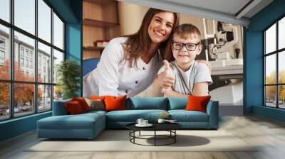 Female eye doctor sitting with the kid after doing the vision test Wall mural