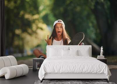 Front view, showing gestures. Happy little girl with skateboard outdoors Wall mural