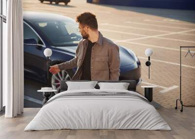 Front view. Man is standing near his electric car outdoors Wall mural