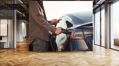 Grey colored formal clothes. Man is standing near his electric car outdoors Wall mural