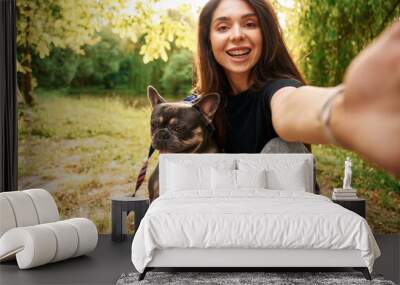 Hand holding camera, doing selfie. Young pretty woman is with her dog in the park Wall mural