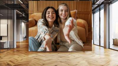 Having fun, sitting. Two happy young female best friends are indoors Wall mural