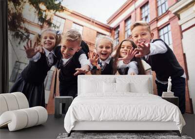 Having fun and embracing each other. Group of kids in school uniform that is outdoors together near education building Wall mural