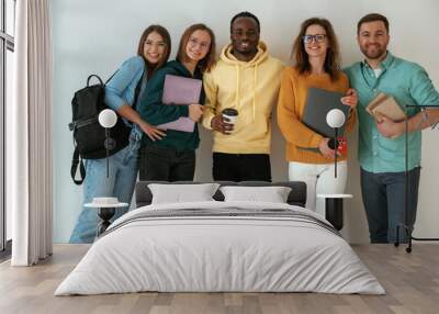 Holding notepads and coffee cup. Group of young people are standing against white background Wall mural