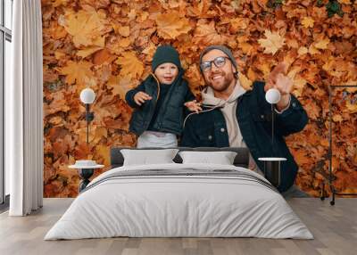 Laying down on the ground that covered with fallen leaves. Father and young son is together outdoors at daytime Wall mural