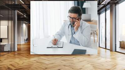 Man giving information by phone. Professional medical worker in white coat is in the office Wall mural