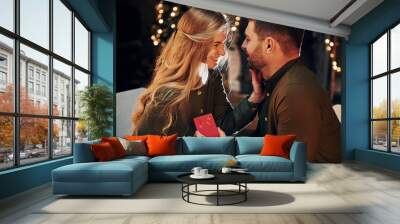 Man holds gift box. Makes proposal mo marry him. Young lovely couple have romantic dinner indoors together Wall mural