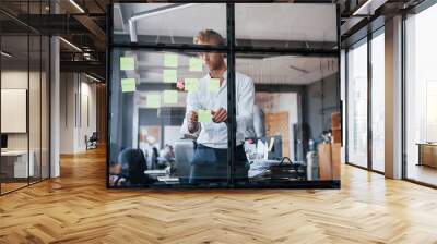 Man in formal clothes stands in the office behind the glass and puts stickers on it Wall mural