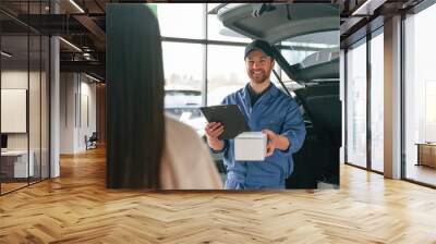 Man is holding box and notepad. Young woman is visiting auto mechanic in garage. Repair service Wall mural