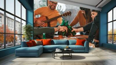 Man is playing guitar. Group of friends is having good weekend indoors in the wooden building together Wall mural