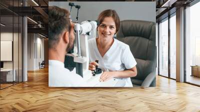 Modern technologies. Man's vision checked by female doctor in the clinic by using special optometrist device Wall mural