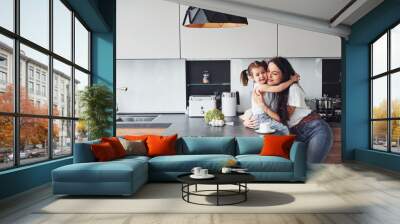 Mother with her little daughter embracing each other indoors in kitchen Wall mural