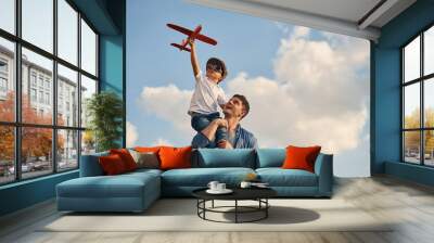 Orange colored toy plane in hands. Father and little son are playing and having fun outdoors Wall mural