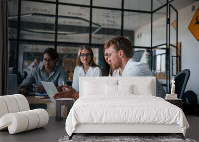 Sits by the table with laptops. Young business people in formal clothes working in the office Wall mural